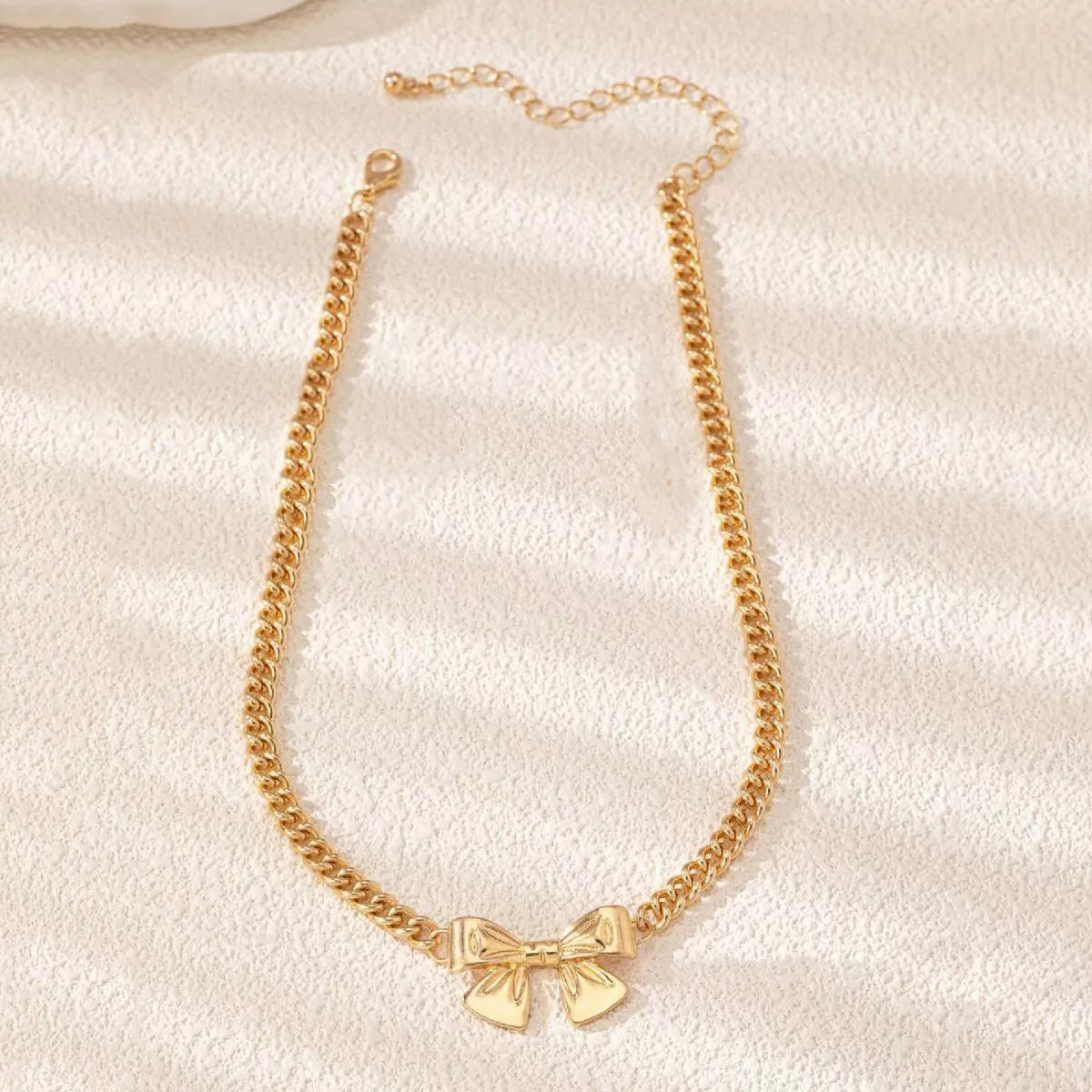 Flatlay view of 18K gold-plated bowknot necklace showing full chain layout and lobster clasp.