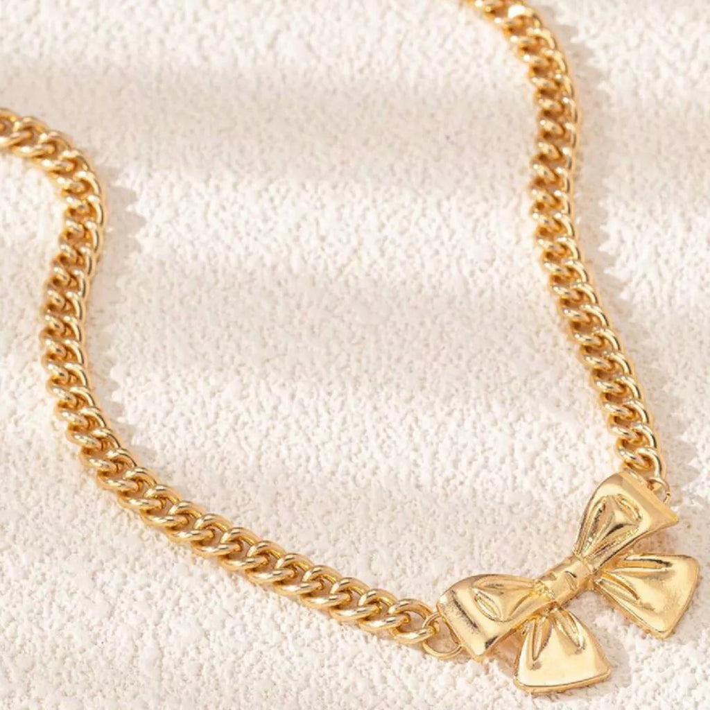 Close-up details of the sculpted 18K gold-plated bowknot center charm and curb chain links.