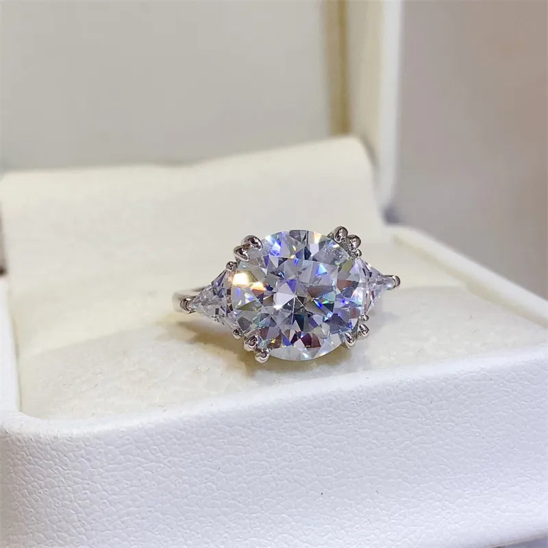 Angled front view of 5 carat round moissanite ring with trillion side accents in box.