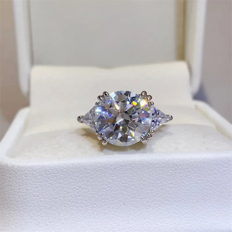 Three-stone 5 carat round moissanite ring displayed in white presentation box.