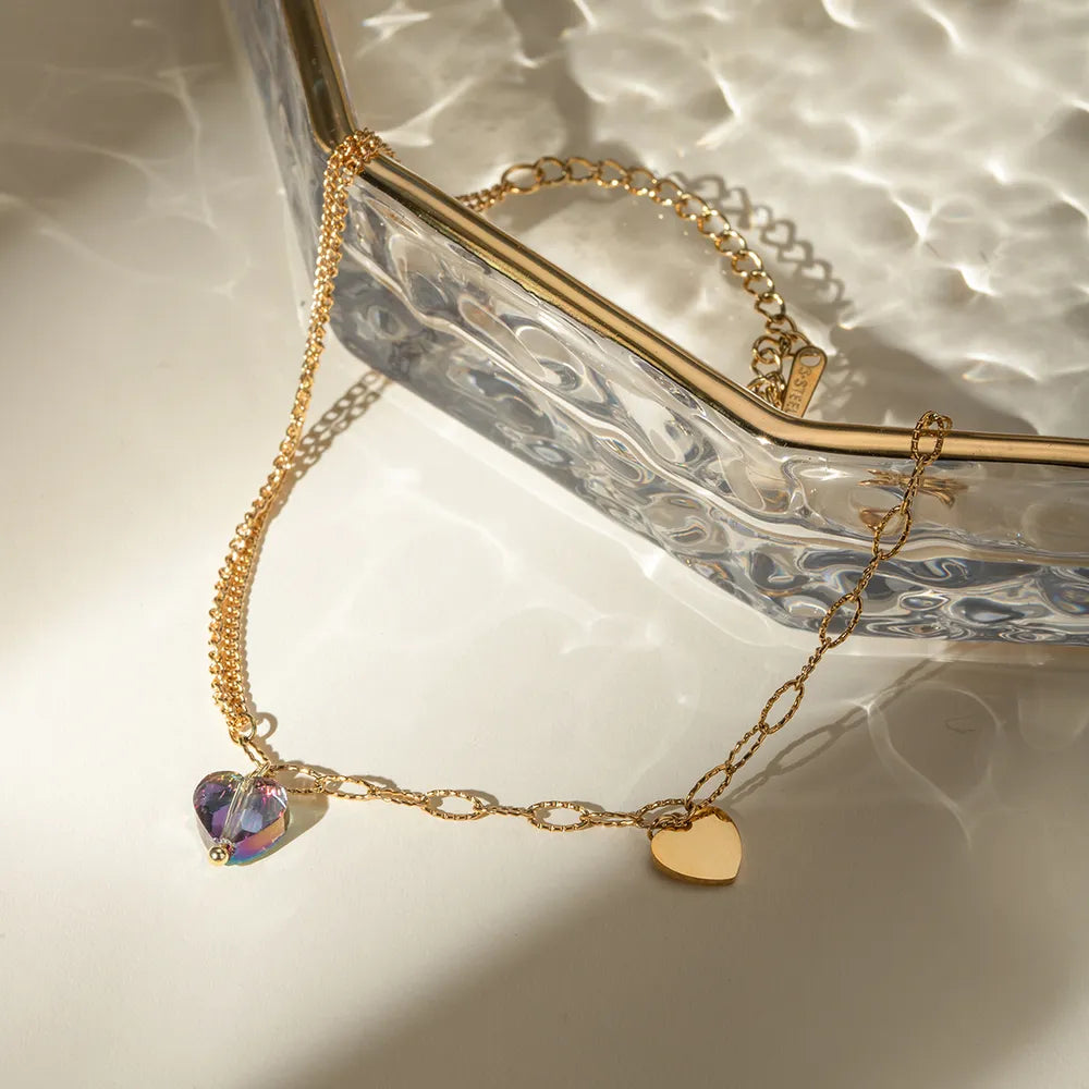 Close-up of iridescent crystal heart pendant and gold heart charm on glass surface