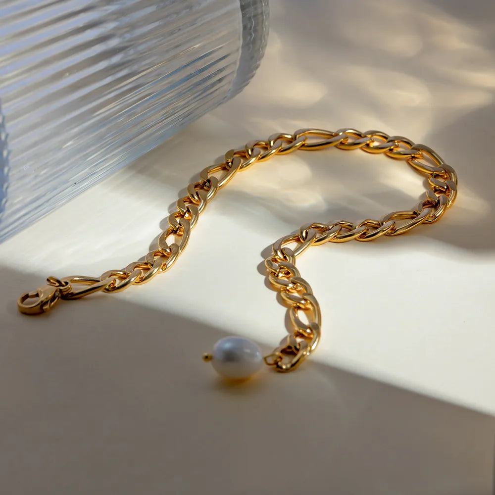 Elegant gold-plated pearl anklet placed next to ribbed glass
