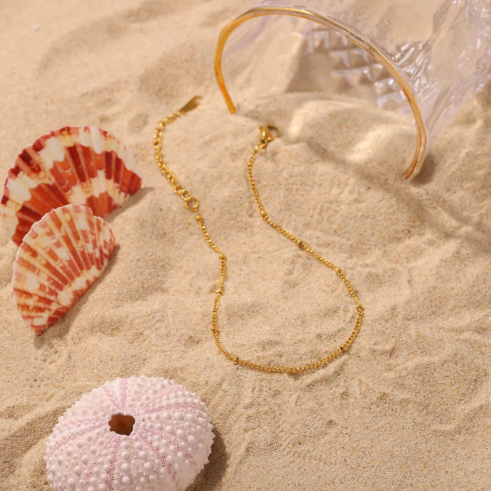 Gold-plated bead anklet on beach sand with sea shells and glass