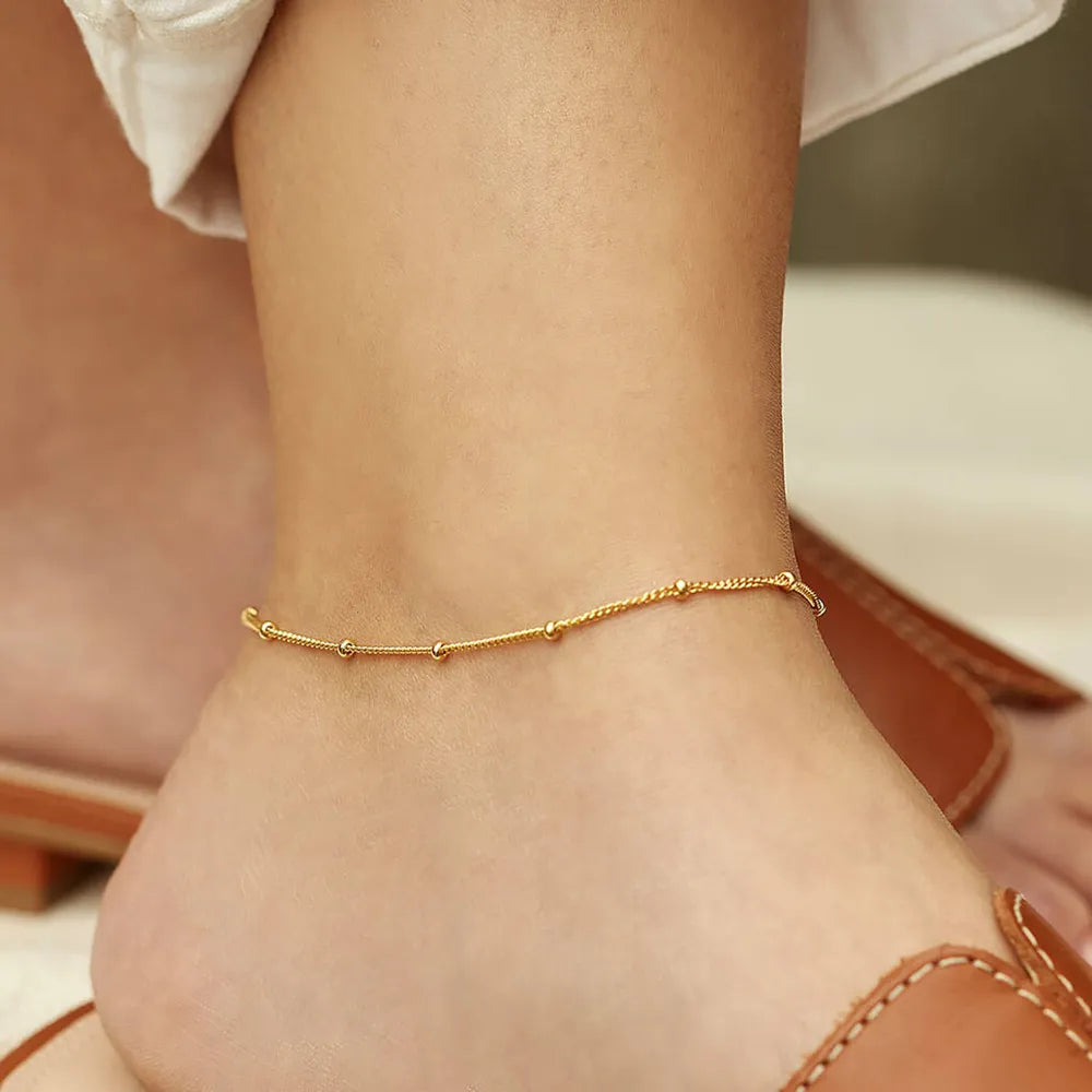 Woman wearing gold-plated bead anklet on ankle with brown sandals
