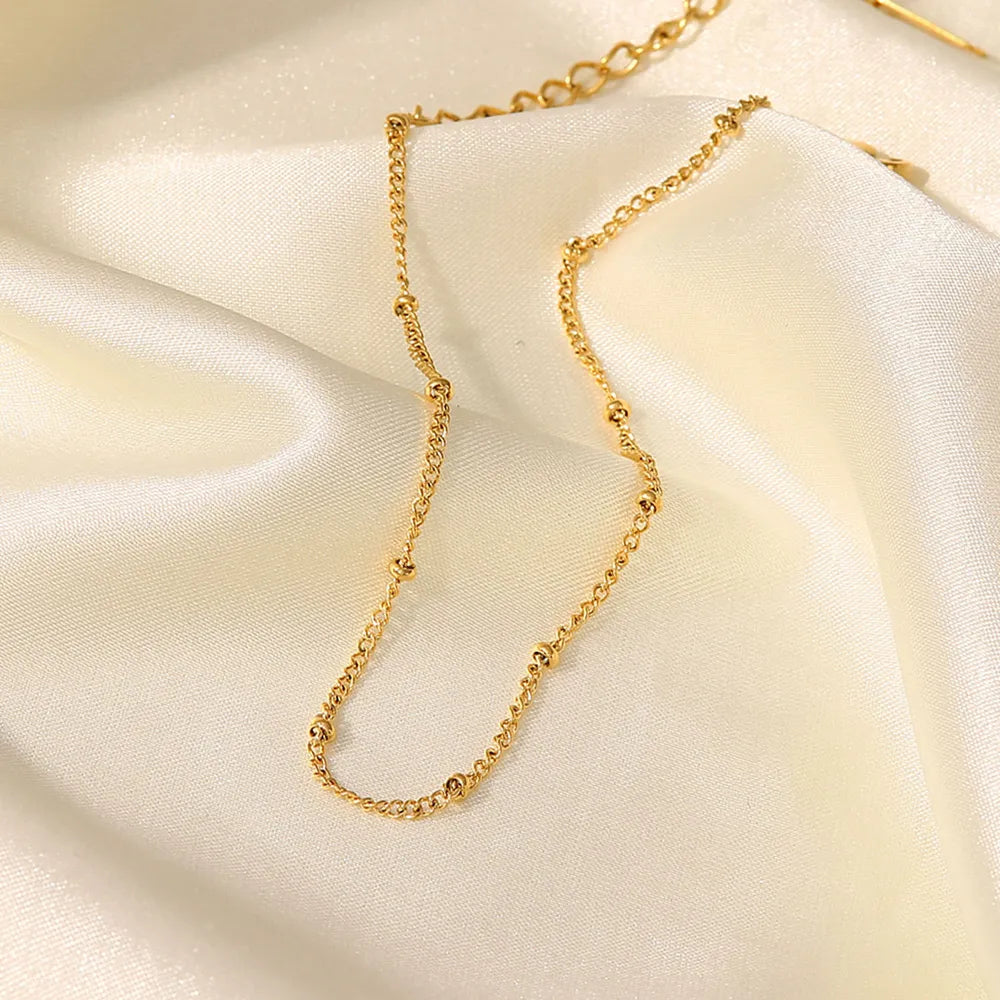 Gold-plated bead chain anklet on smooth white silk fabric