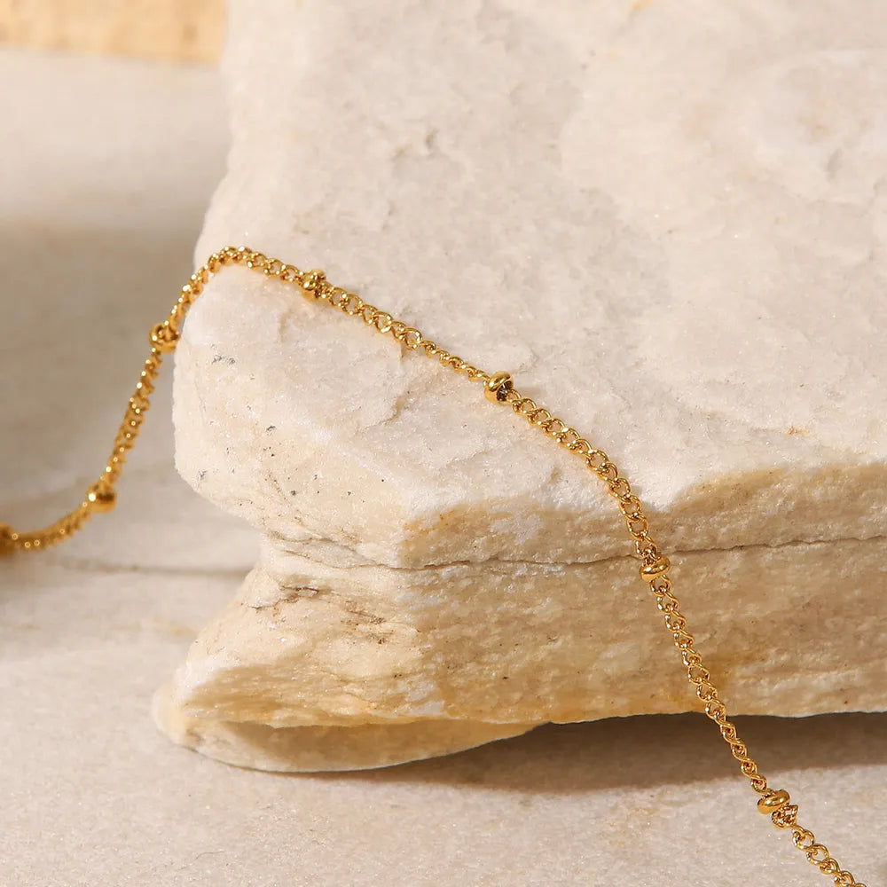 Close up of gold-plated beaded chain link on natural stone surface