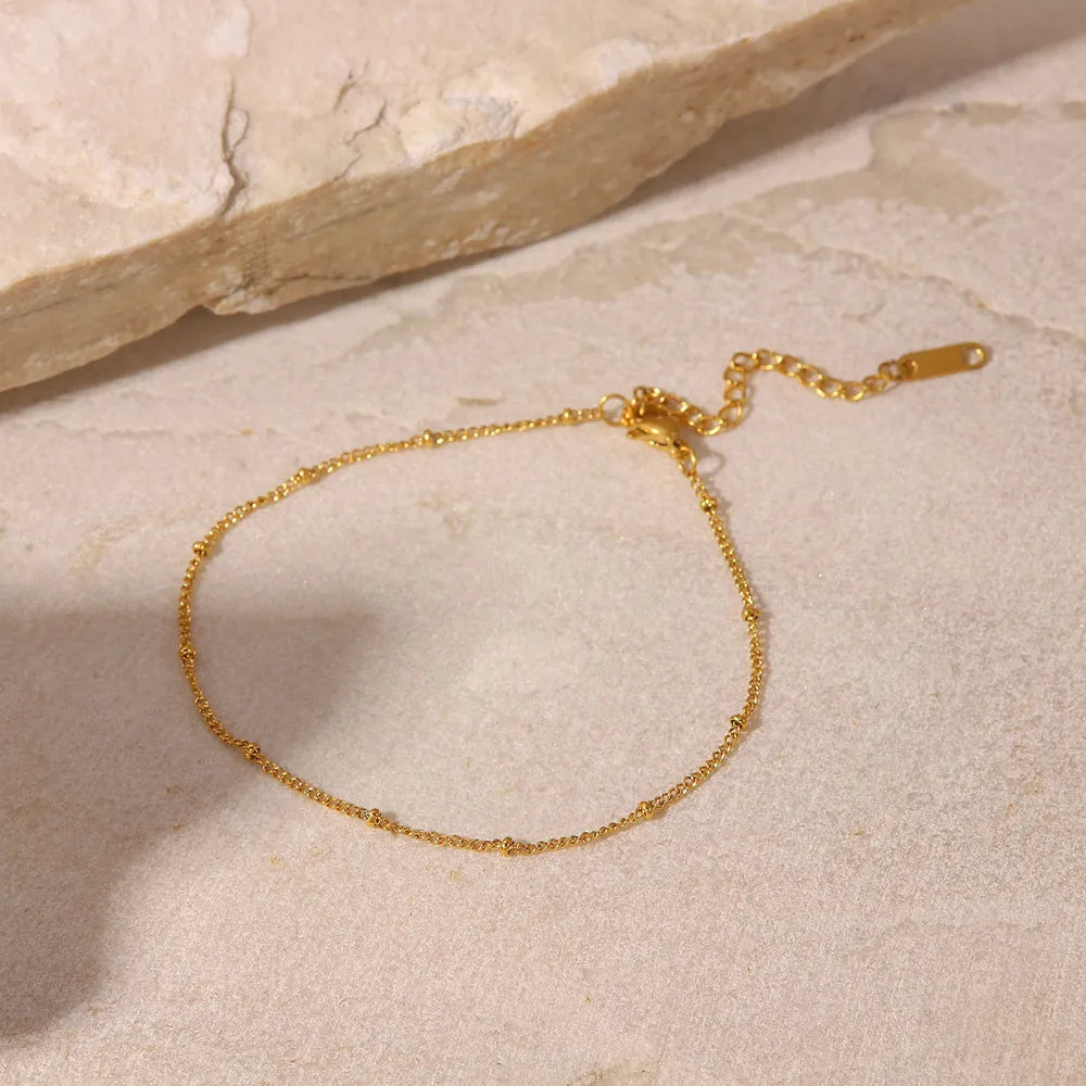 Delicate gold-plated bead anklet displayed on neutral stone background