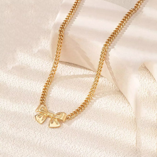Gold-plated bowknot Cuban chain necklace displayed on a textured aesthetic pedestal.