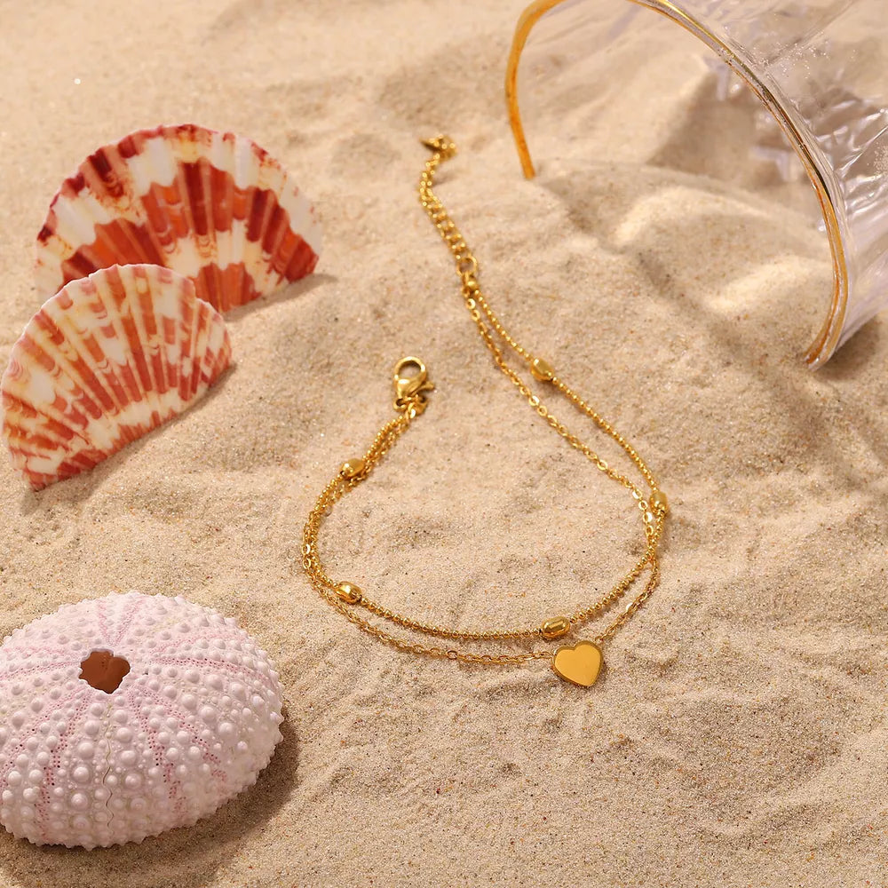 Gold-plated heart anklet on beach sand with sea shells