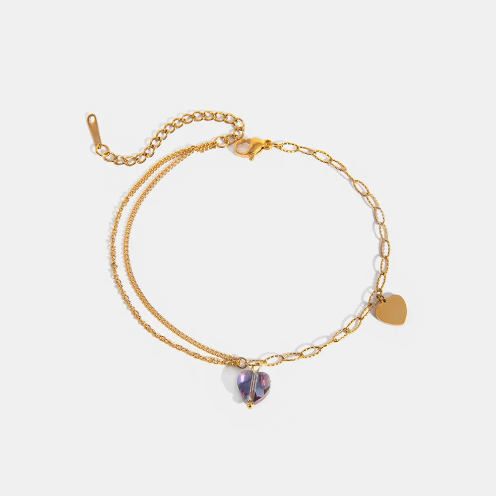 Layered gold-plated stainless steel anklet with purple crystal heart pendant and gold heart charm on plain white background