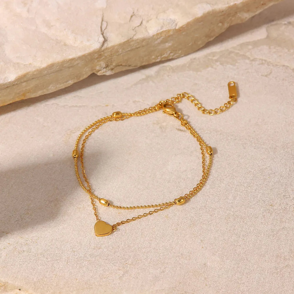Double layered gold-plated heart anklet displayed on neutral stone background
