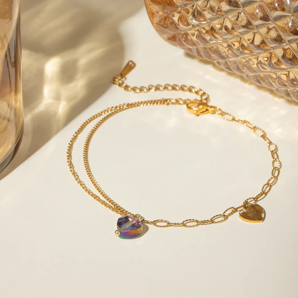 Double-layered gold-plated chain anklet featuring crystal heart charm under warm aesthetic lighting