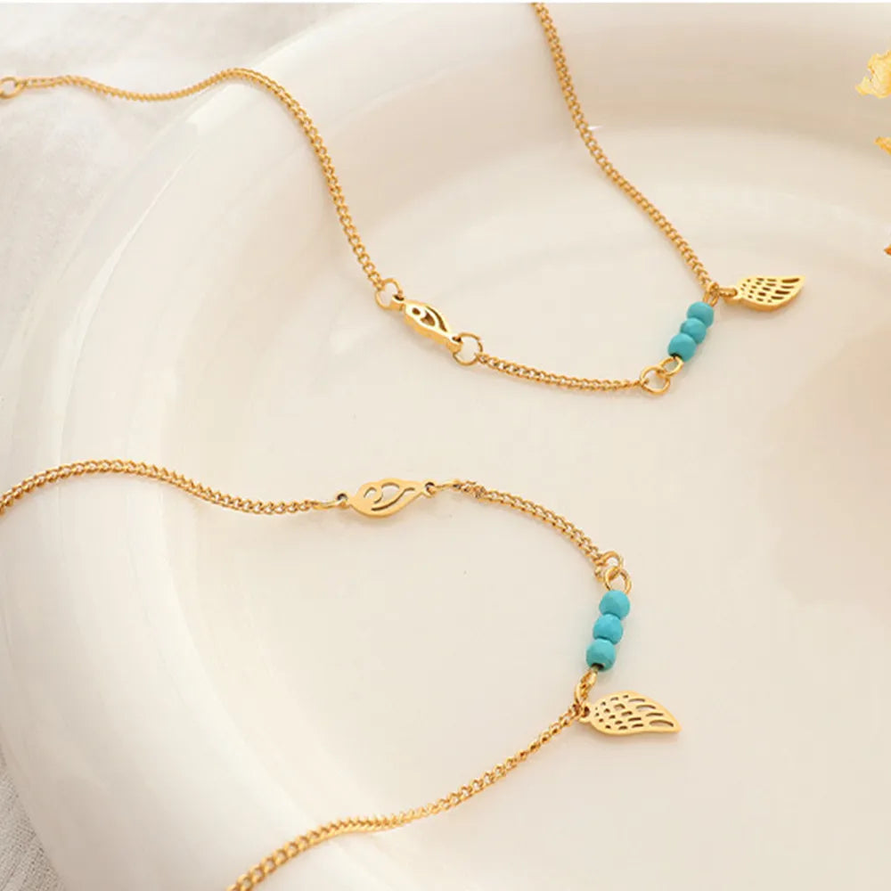 Fine gold wing anklets displayed inside white ceramic dish under warm sunlight