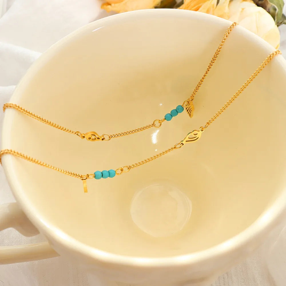 Gold charm anklets draped over edge of cream ceramic tea cup