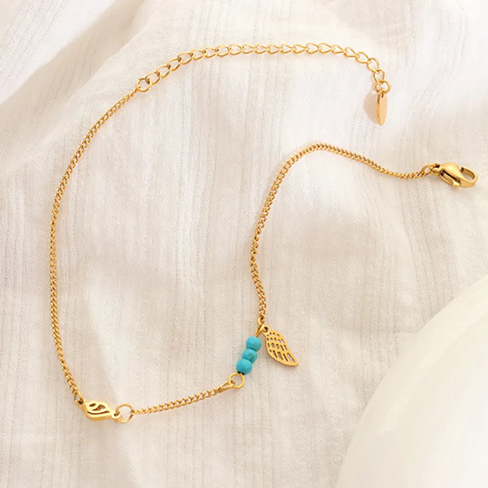 Gold wing charm anklet displayed flat on textured white linen fabric