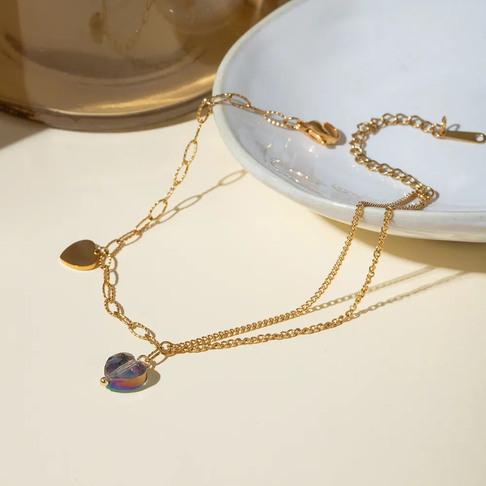 Stainless steel crystal heart anklet displayed on white ceramic dish with soft sunlight shadows