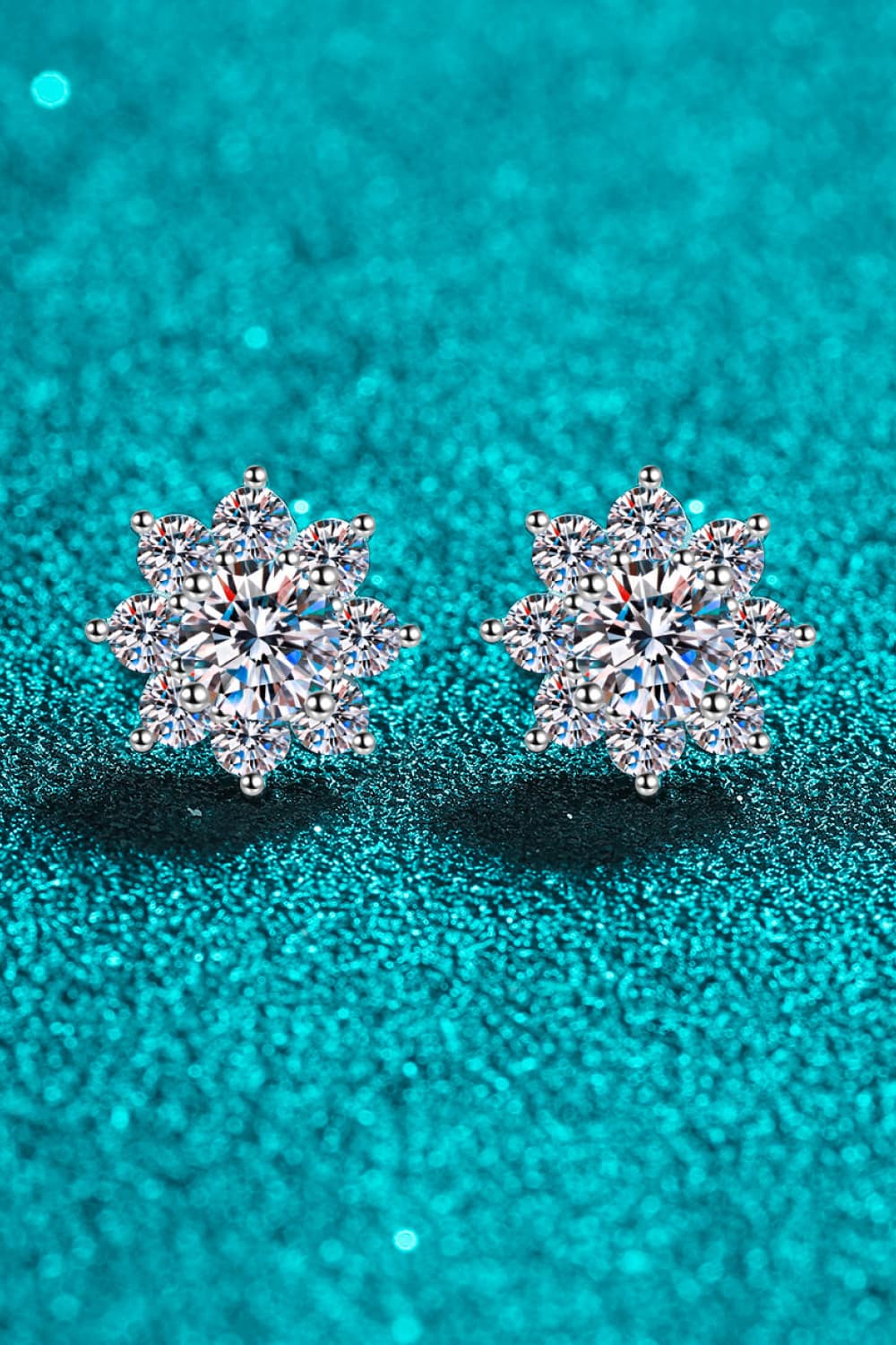 Front view of silver moissanite floral halo stud earrings on sparkling teal background.