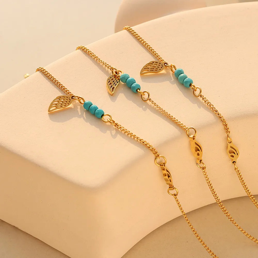 Gold wing and turquoise beaded anklets laid across warm beige display block