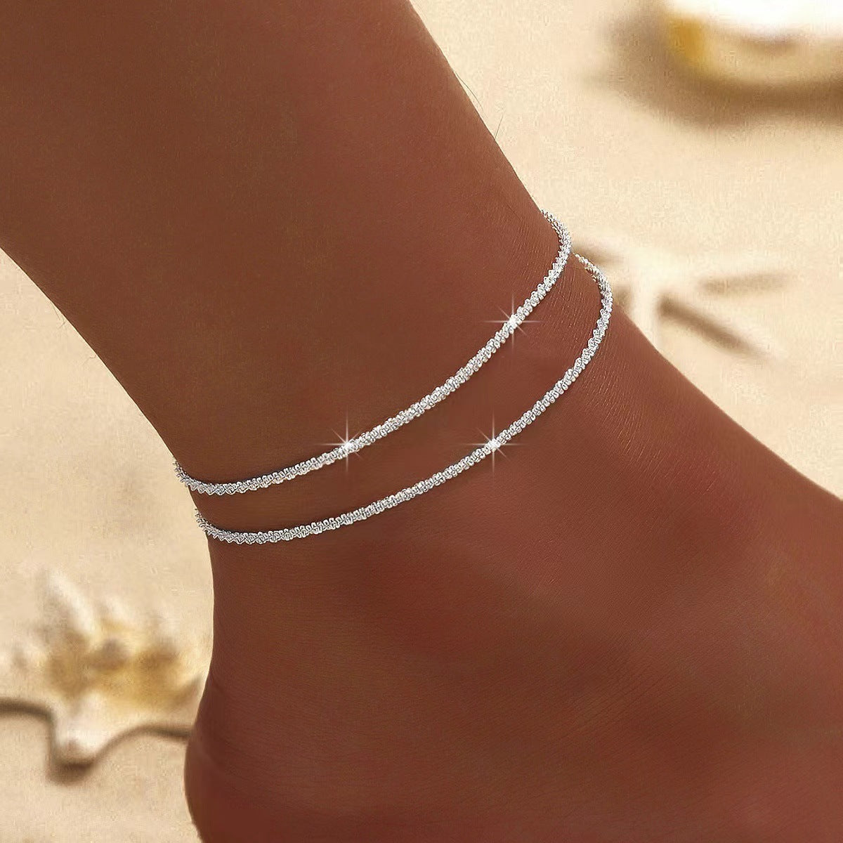 Woman wearing silver-tone layered anklet on a sunny beach background