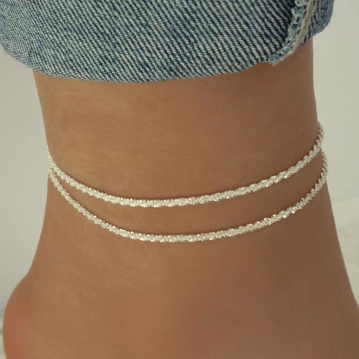 Silver-tone double layer sparkle anklet worn on ankle with denim jeans background